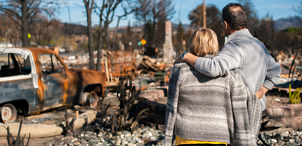 blog-featured_natural_disaster-1030x500 A middle-aged couple looks on at the damage done by a natural disaster