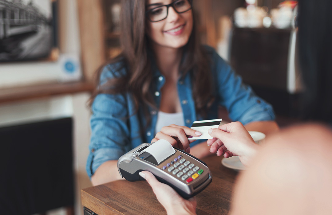 A woman with glasses uses a credit card to make a purchase at a small business