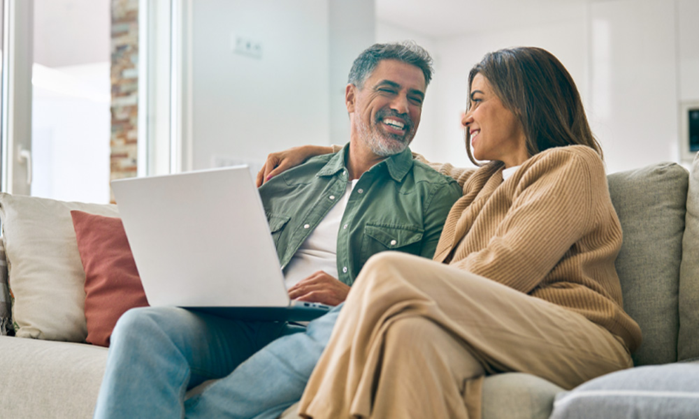 Happy couple sitting on couch looking at a laptop.