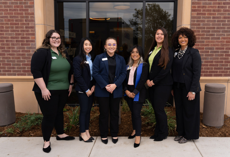 A team of six female INTRUST Bank employees standing outside of a banking center