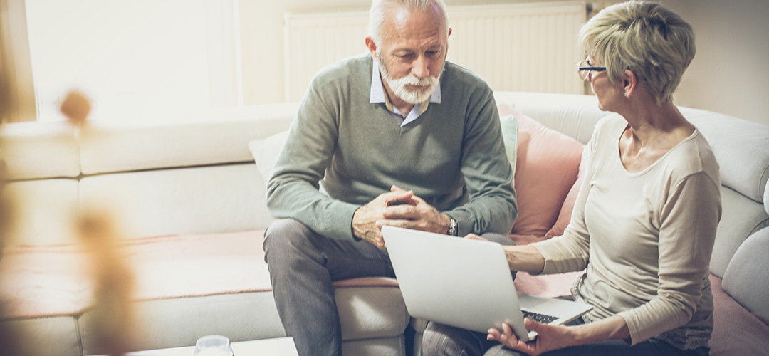 blog-featured_reaching-retirement_1080x500 A mature couple sitting on a couch looking at a laptop screen